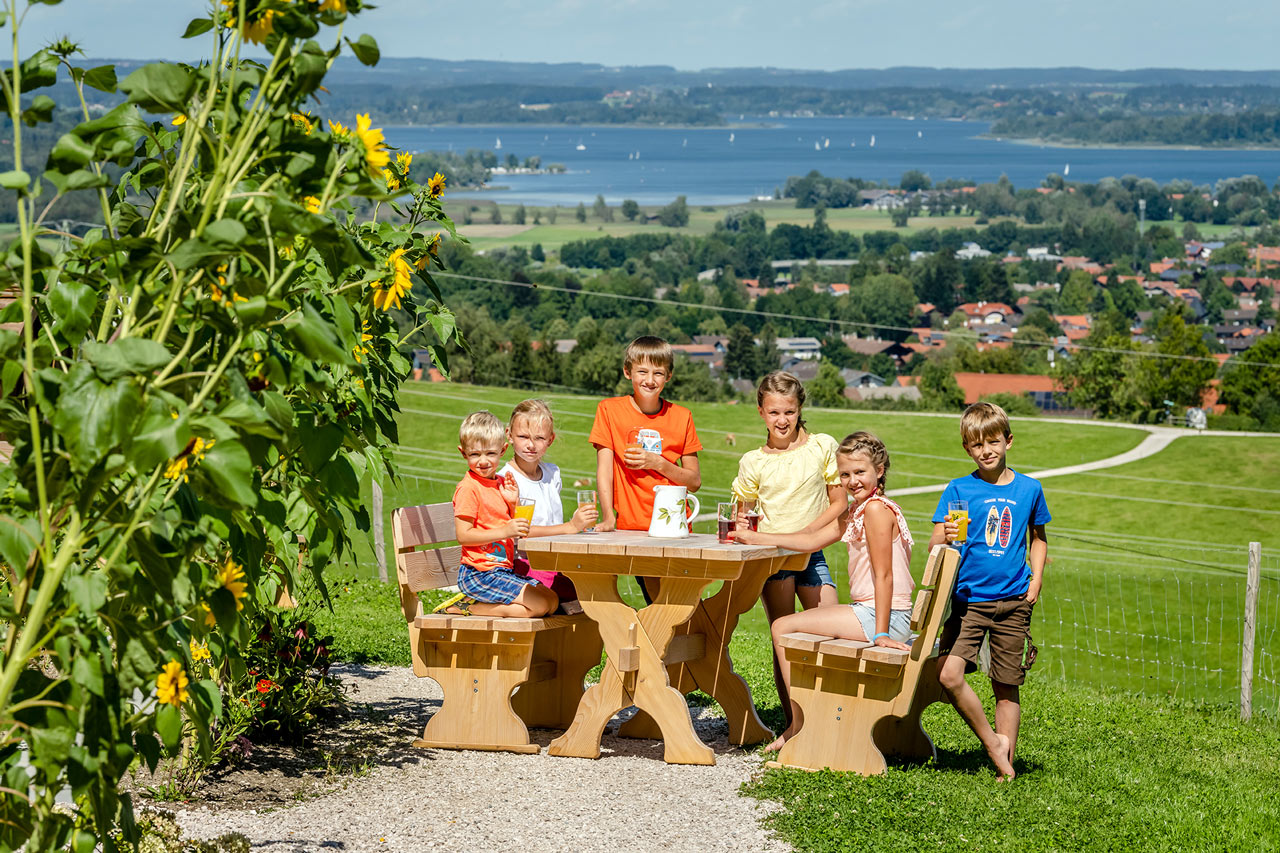 Eine Familie am Tisch vor einem Chiemsee Bauernhof mit Blick auf den See